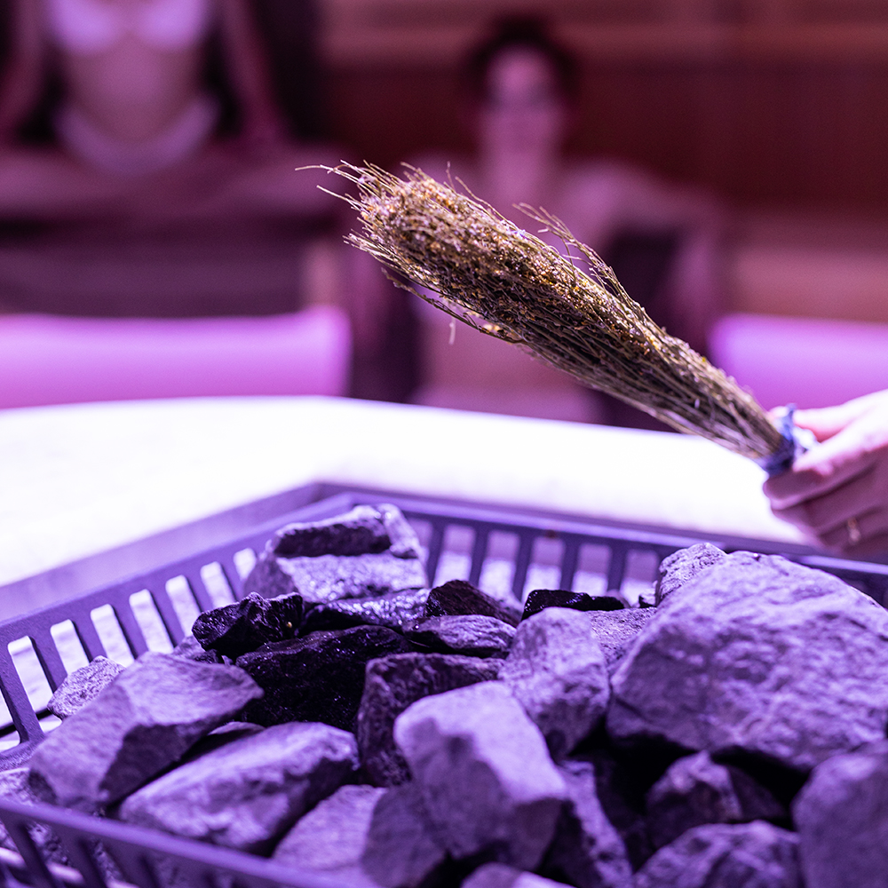 A close-up of sauna stones with a person holding a herbal whisk